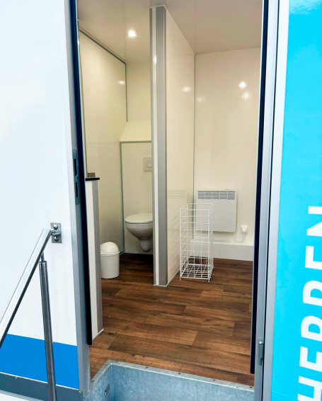 WC-Wagen Riese von innen, weiße Miet-Toilette mit laminat in Holzoptik und weißen Toiletten